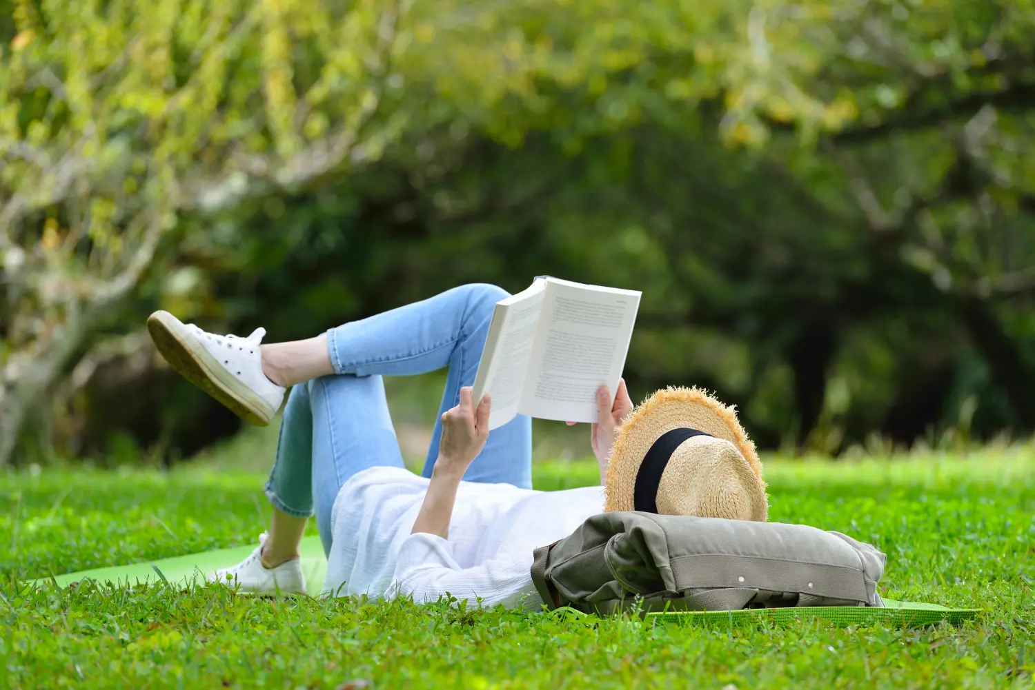 Frau liegt auf grünem Gras und liest ein Buch